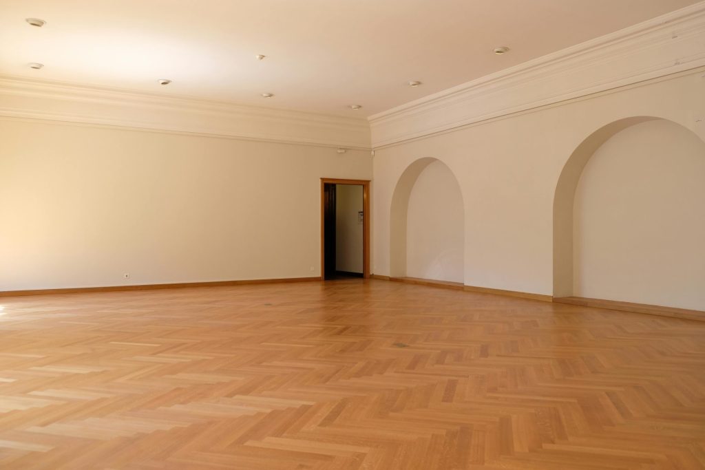 Une grande pièce vide avec un élégant parquet, des arches et une lumière naturelle, idéale pour trouver l'inspiration en matière de décoration intérieure.