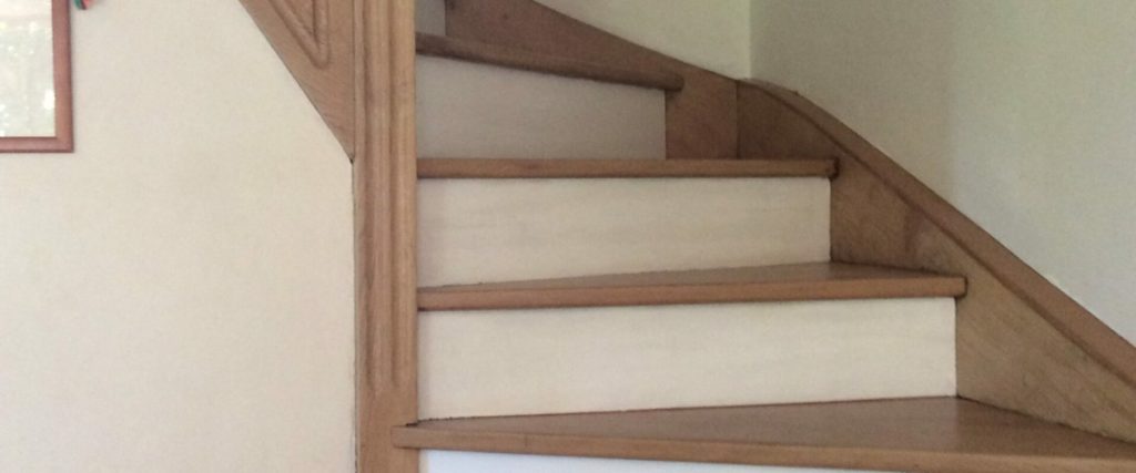 Un escalier en bois avec un mur blanc et une porte blanche en arrière-plan.