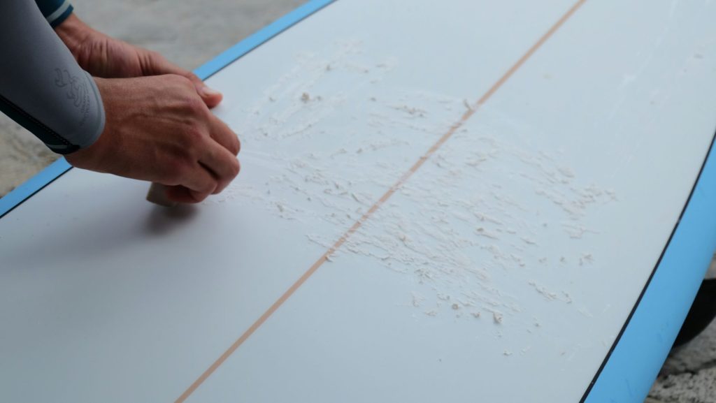 Une personne tient une planche de surf sur laquelle il y a des inscriptions.